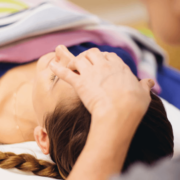 Person lying down with their eyes closed, receiving gentle hand placement on the forehead as part of a therapeutic session.